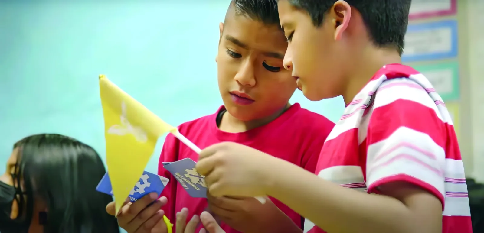 Two boys huddle close together reading a Starforce card